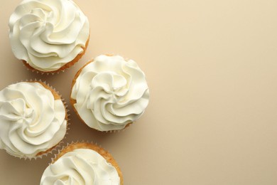 Photo of Tasty vanilla cupcakes with cream on beige background, top view. Space for text