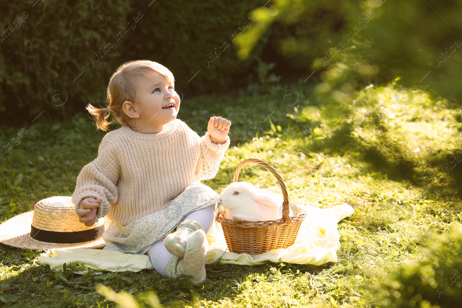 Photo of Happy little girl with cute rabbit on green grass outdoors