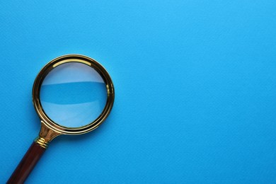 Photo of Magnifying glass on light blue background, top view. Space for text