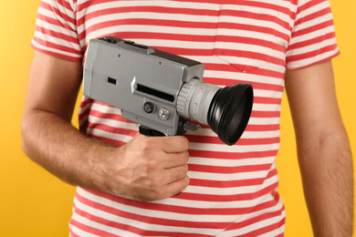Man with vintage video camera on yellow background, closeup