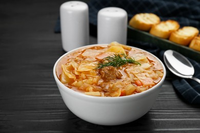 Tasty cabbage soup with meat, carrot and dill on black wooden table, closeup