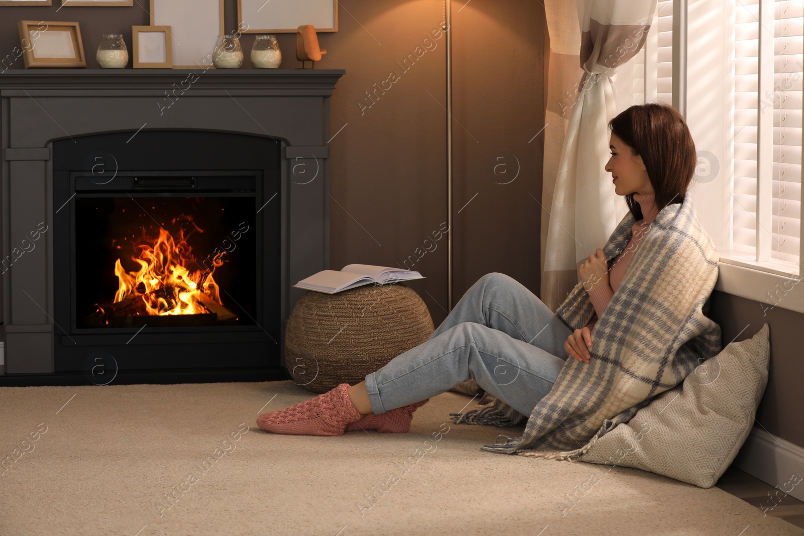 Photo of Beautiful young woman sitting on floor near fireplace at home. Space for text