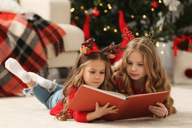 Photo of Cute little girls reading book at home. Christmas atmosphere