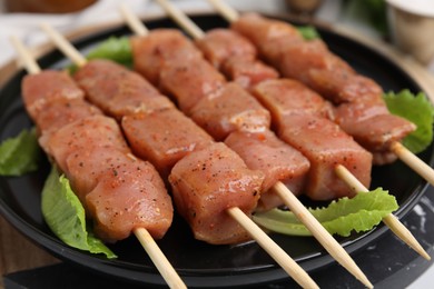 Photo of Wooden skewers with cut raw marinated meat on plate, closeup