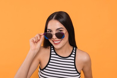 Photo of Attractive happy woman touching fashionable sunglasses against orange background