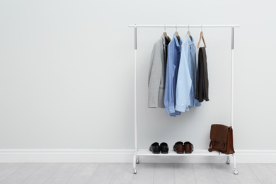 Photo of Rack with stylish men's clothes in room. Space for text