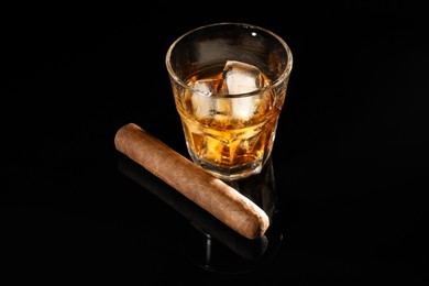 Photo of Glass of whiskey with ice cubes and cigar on black mirror surface