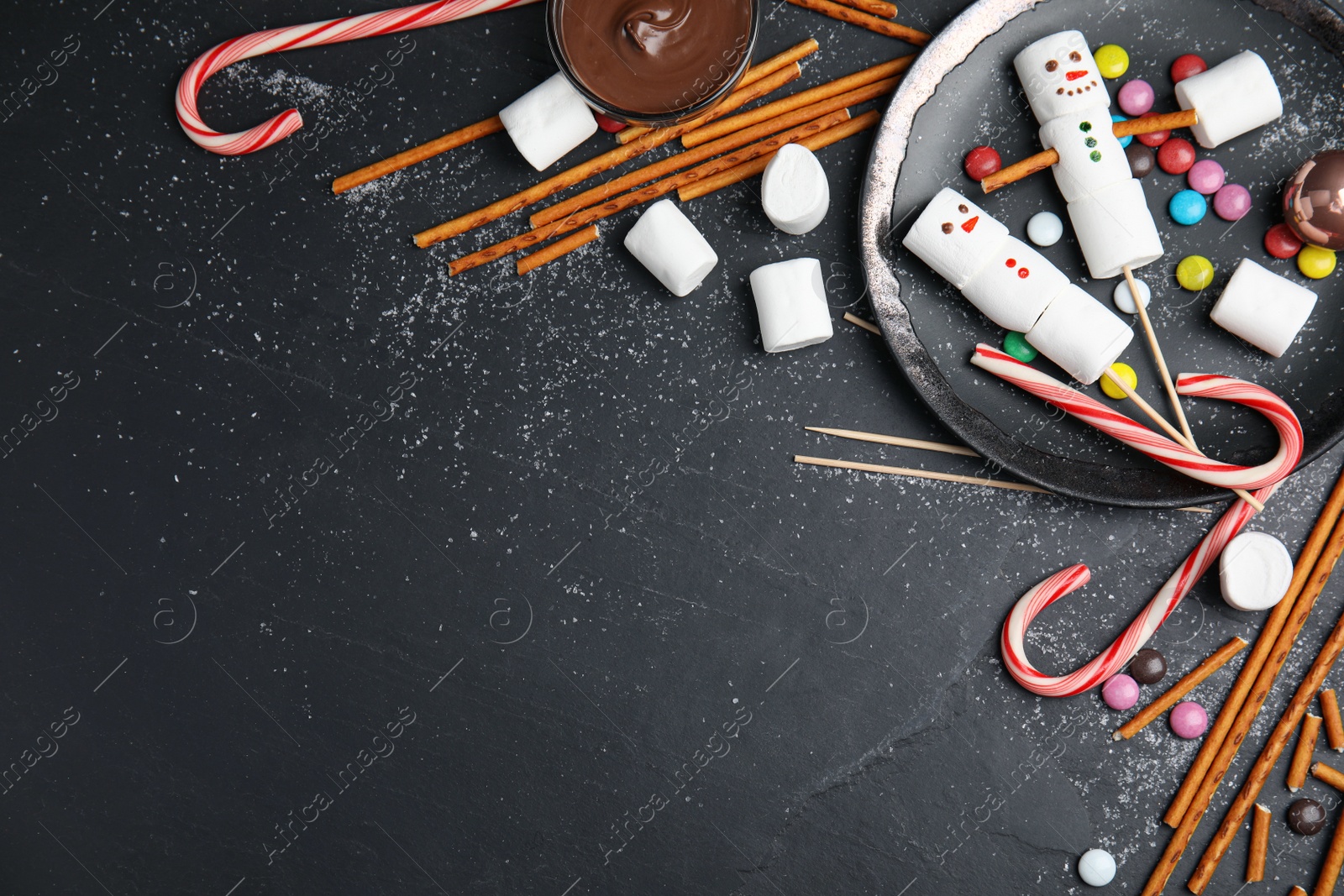 Photo of Flat lay composition with funny snowmen made of marshmallows on black table. Space for text