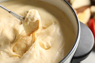 Dipping piece of bread into fondue pot with melted cheese on grey background, closeup