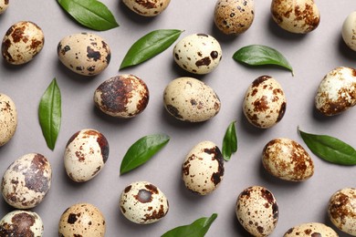 Photo of Speckled quail eggs and green leaves on light grey background, flat lay