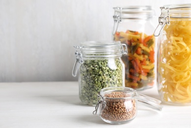 Photo of Jars with buckwheat, peas and pasta on white table. Space for text
