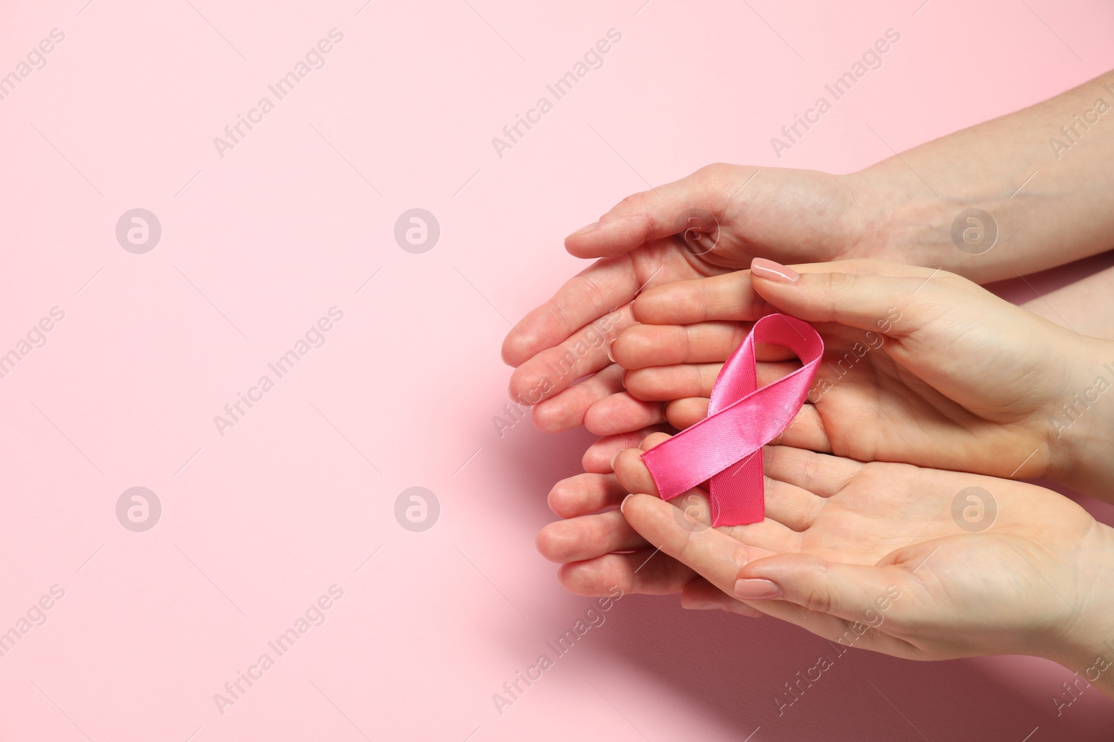 Photo of Breast cancer awareness. Women holding pink ribbon on color background, top view. Space for text