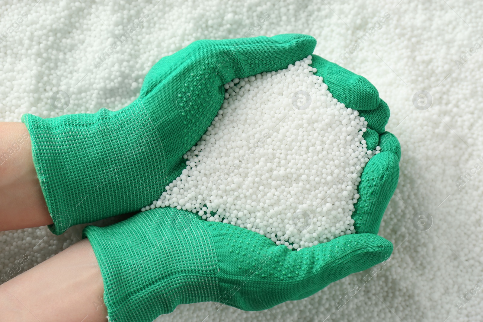 Photo of Farmer holding ammonium nitrate pellets in hands over pile, top view. Mineral fertilizer