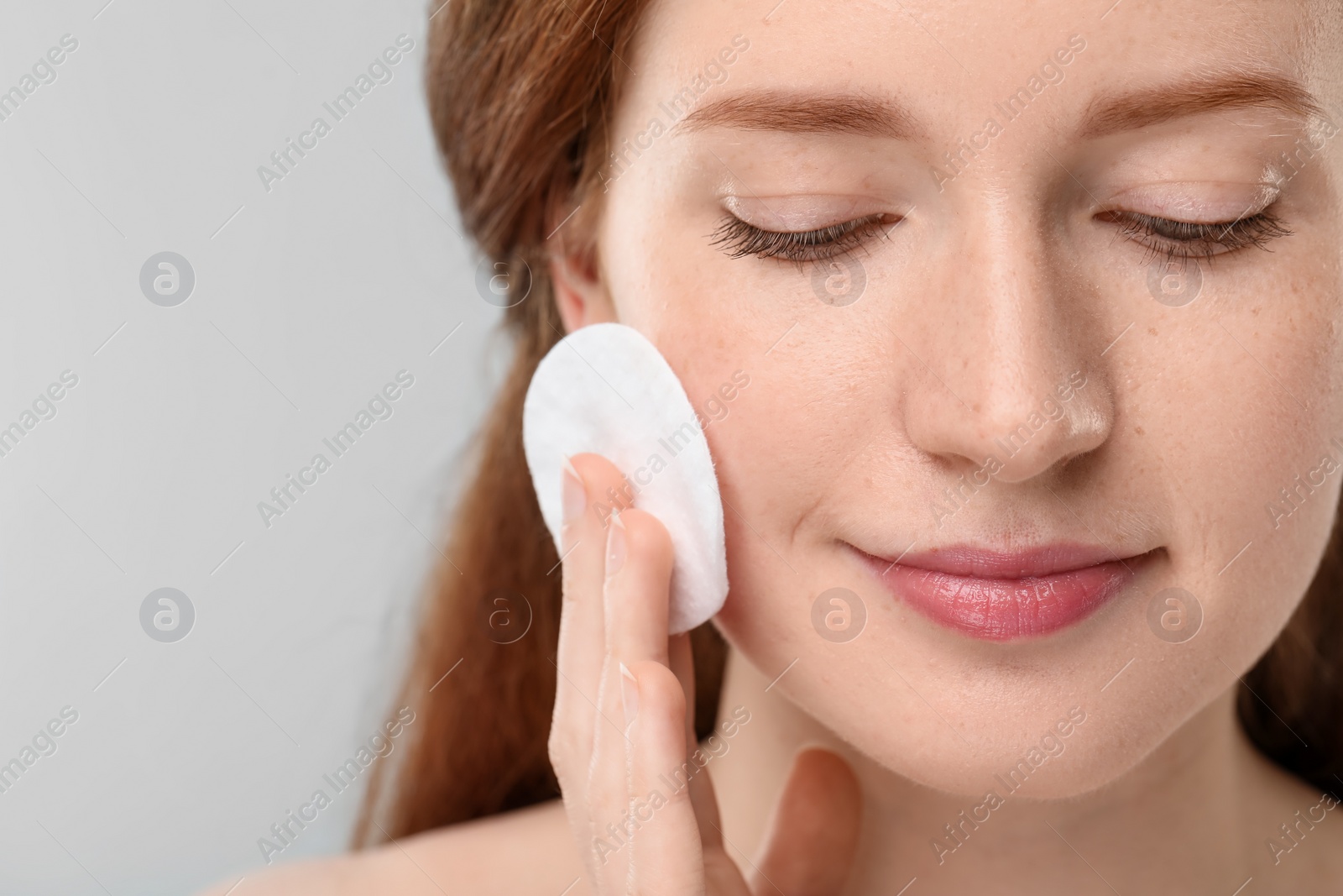 Photo of Beautiful woman with freckles wiping face on grey background, closeup