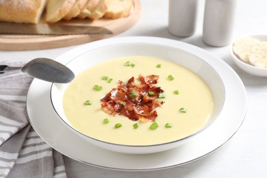 Photo of Tasty potato soup with bacon in bowl and spoon on white table