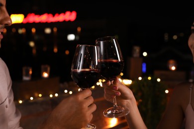 Photo of Romantic couple with glasses of red wine on cafe terrace at night, closeup