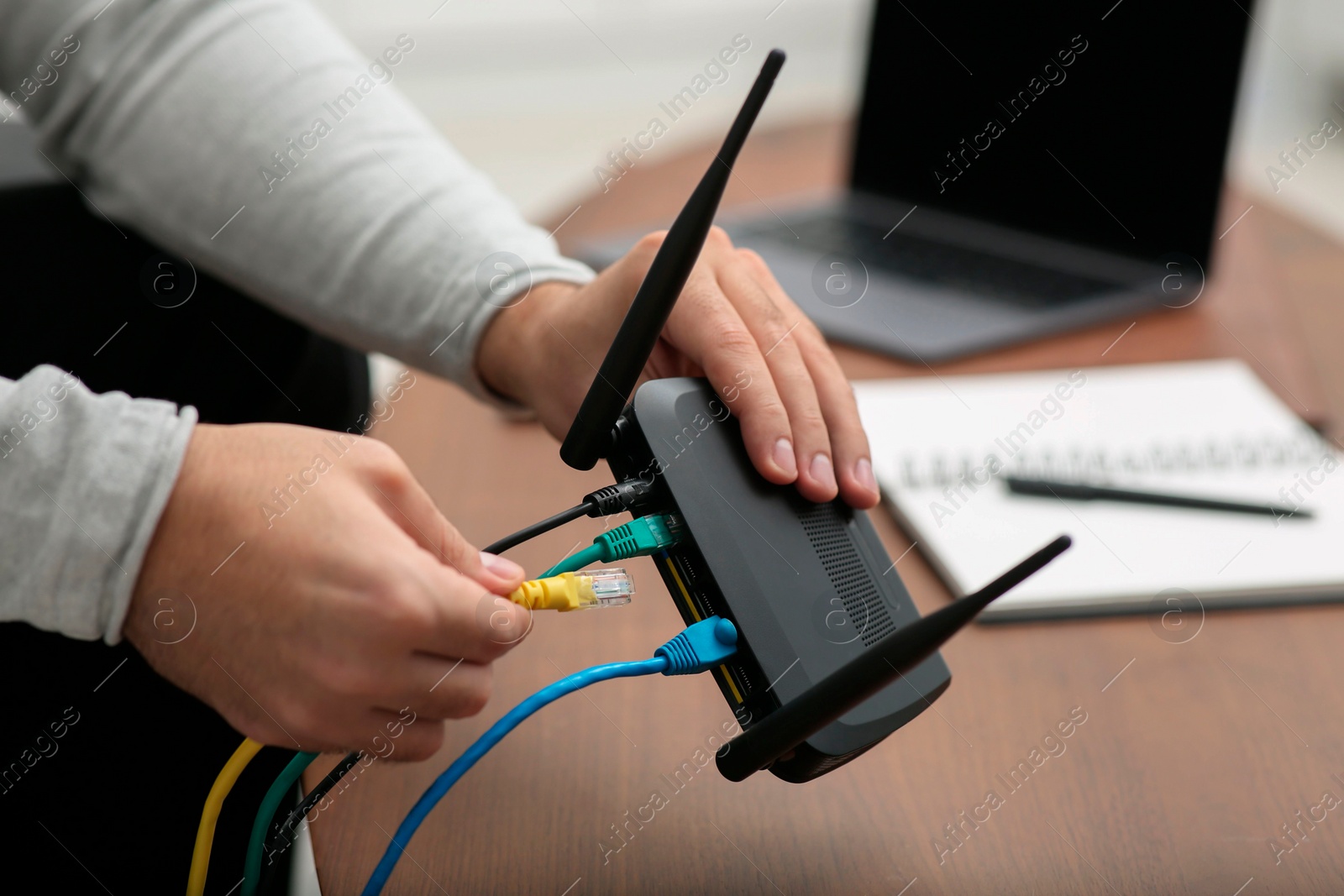 Photo of Man inserting cable into Wi-Fi router at wooden table indoors, closeup