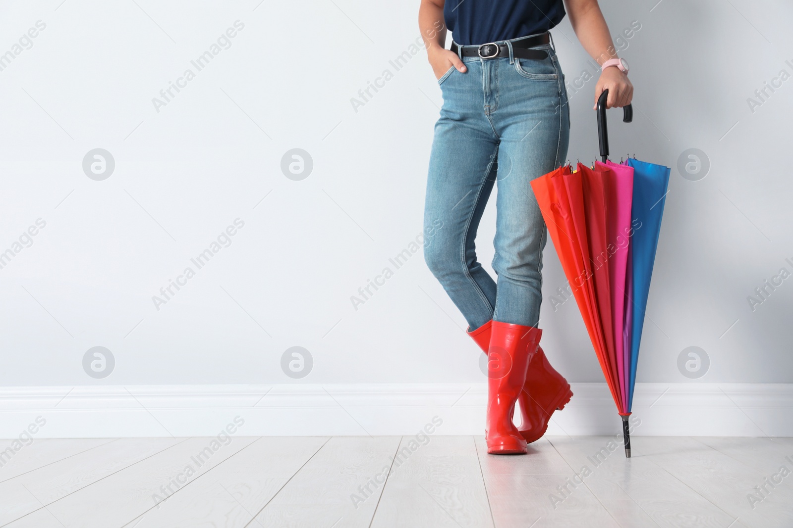 Photo of Woman in gumboots holding bright umbrella near white wall with space for design