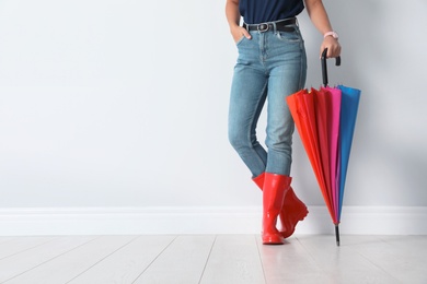 Photo of Woman in gumboots holding bright umbrella near white wall with space for design