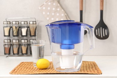 Photo of Water filter jug, glass and lemon on white countertop in kitchen