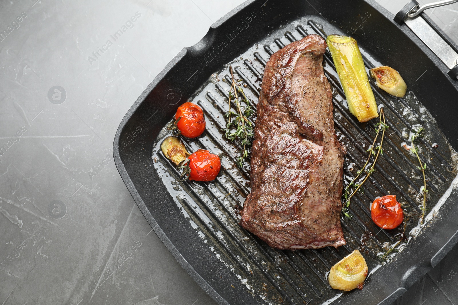 Photo of Delicious grilled beef meat and vegetables in pan on grey table, top view. Space for text