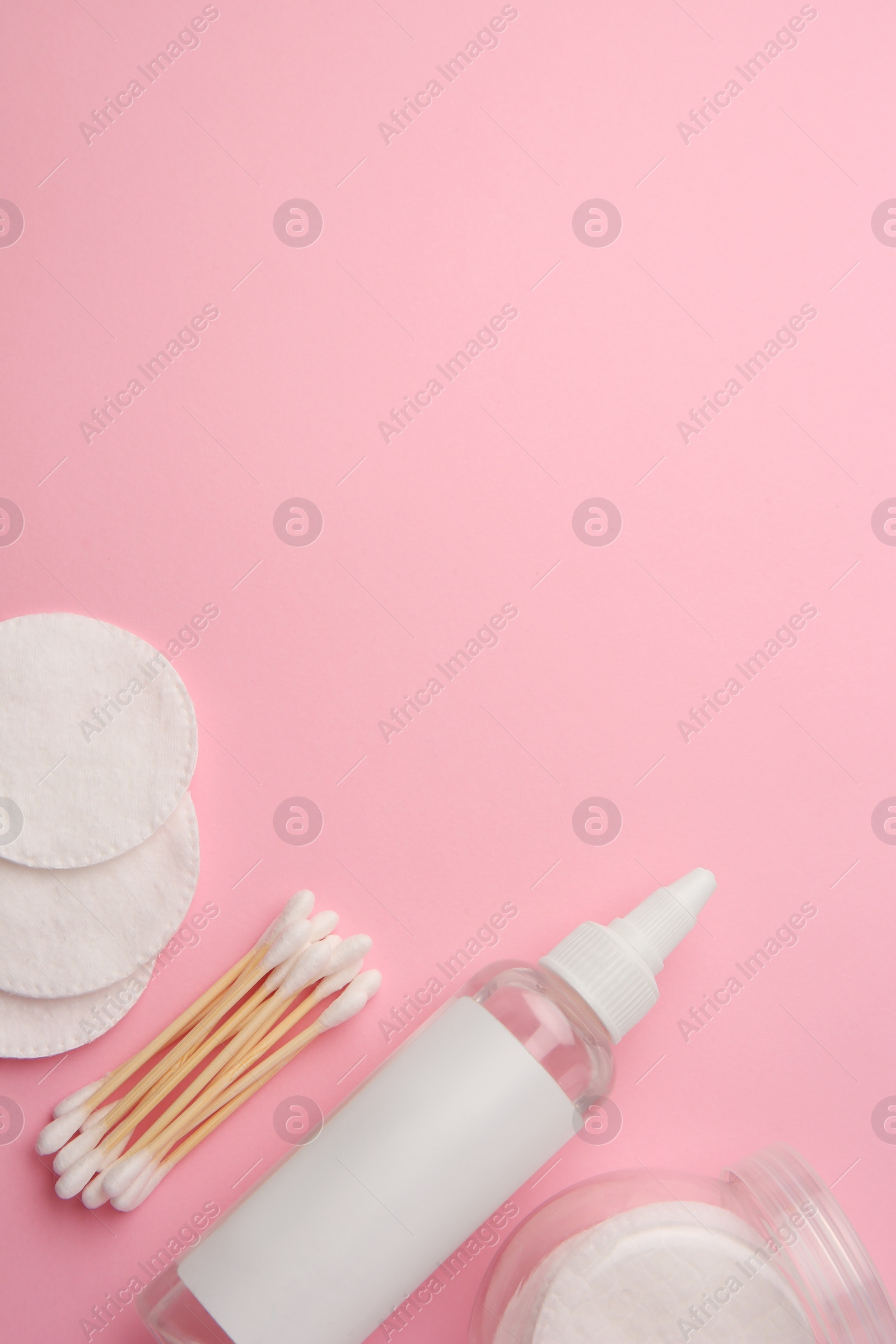 Photo of Bottle of makeup remover, cotton pads and swabs on pink background, flat lay. Space for text