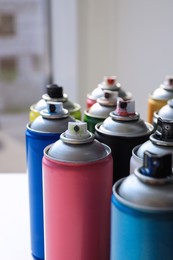Photo of Cans of different graffiti spray paints on table, closeup
