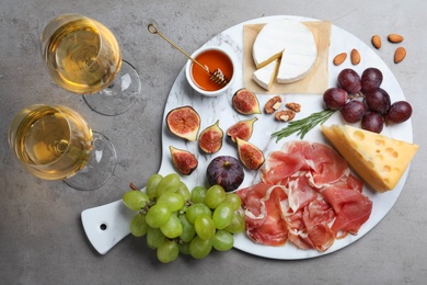 Delicious ripe figs, prosciutto and cheeses served on grey table, flat lay