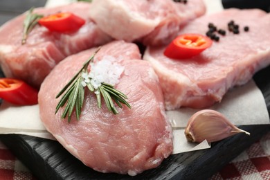 Pieces of raw pork meat with chili pepper and spices on table, closeup