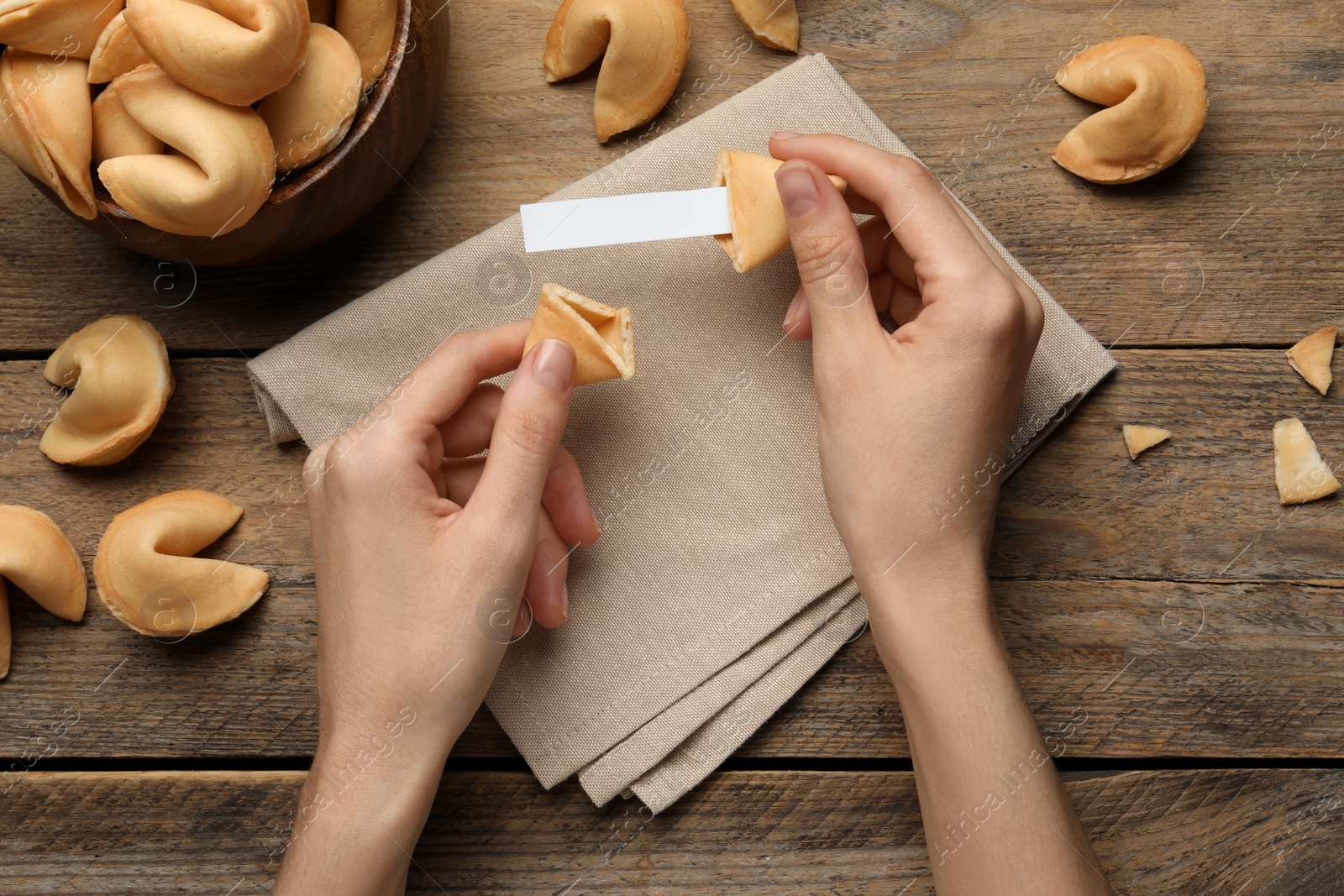 Photo of Woman holding tasty fortune cookie and paper with prediction at wooden table, top view. Space for text