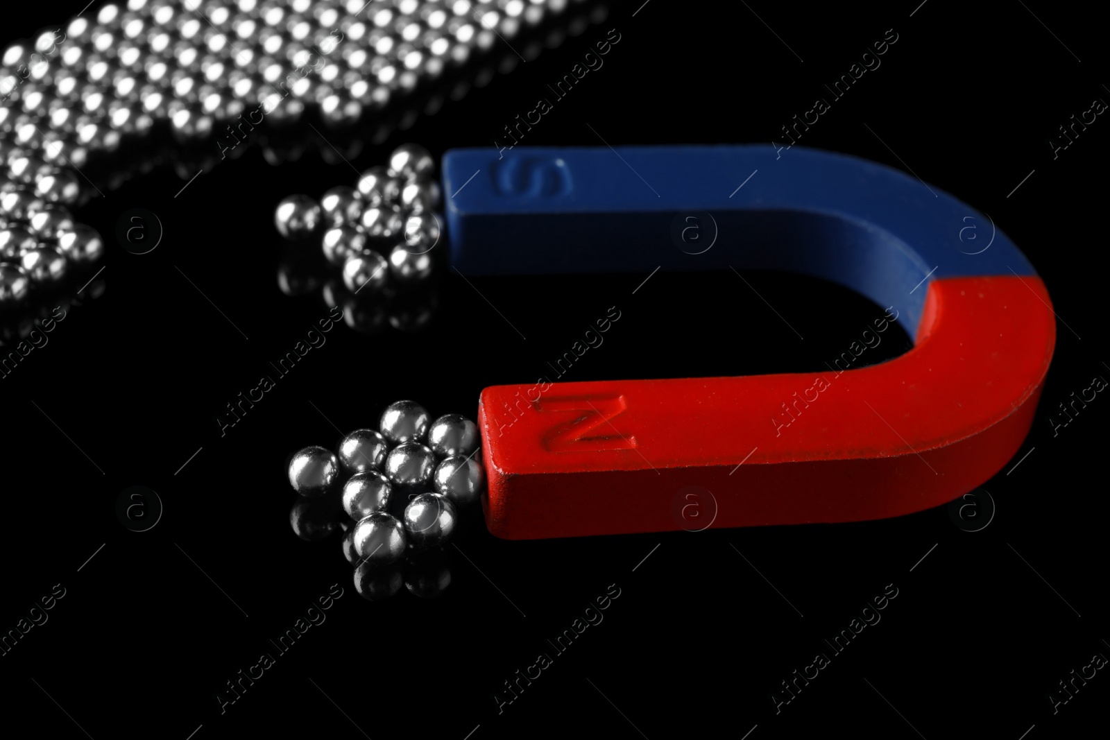 Photo of Magnet attracting chrome balls on black background. Business leadership concept