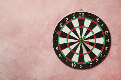 Photo of Dart board with arrows hitting target on pink wall. Space for text