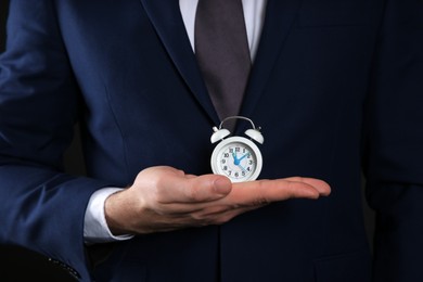Businessman holding tiny alarm clock, closeup. Time management