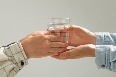 Photo of Caretaker giving glass of water to elderly woman on grey background, closeup