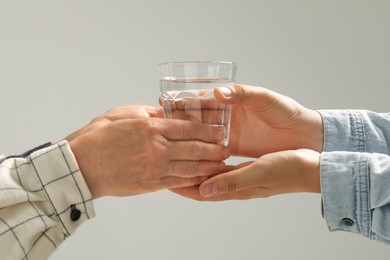 Caretaker giving glass of water to elderly woman on grey background, closeup