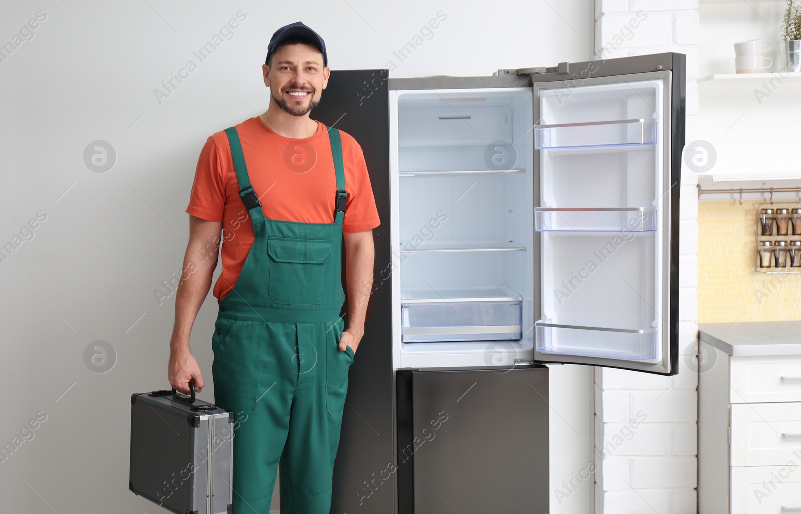 Photo of Male technician with tool box near refrigerator indoors