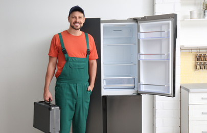 Photo of Male technician with tool box near refrigerator indoors