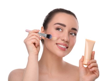 Woman with tube applying foundation on face using brush against white background