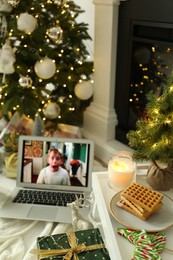 Photo of MYKOLAIV, UKRAINE - DECEMBER 23, 2020: Laptop displaying Home Alone movie near fireplace indoors, focus on tray with cookies and decor. Cozy winter holidays atmosphere
