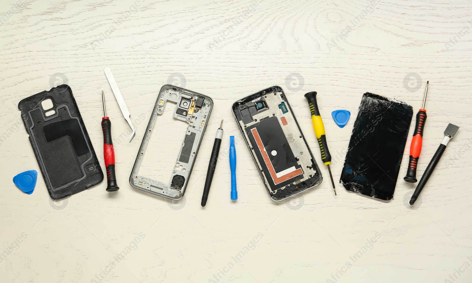 Photo of Parts of damaged smartphone and repair tool set on light beige wooden table, flat lay