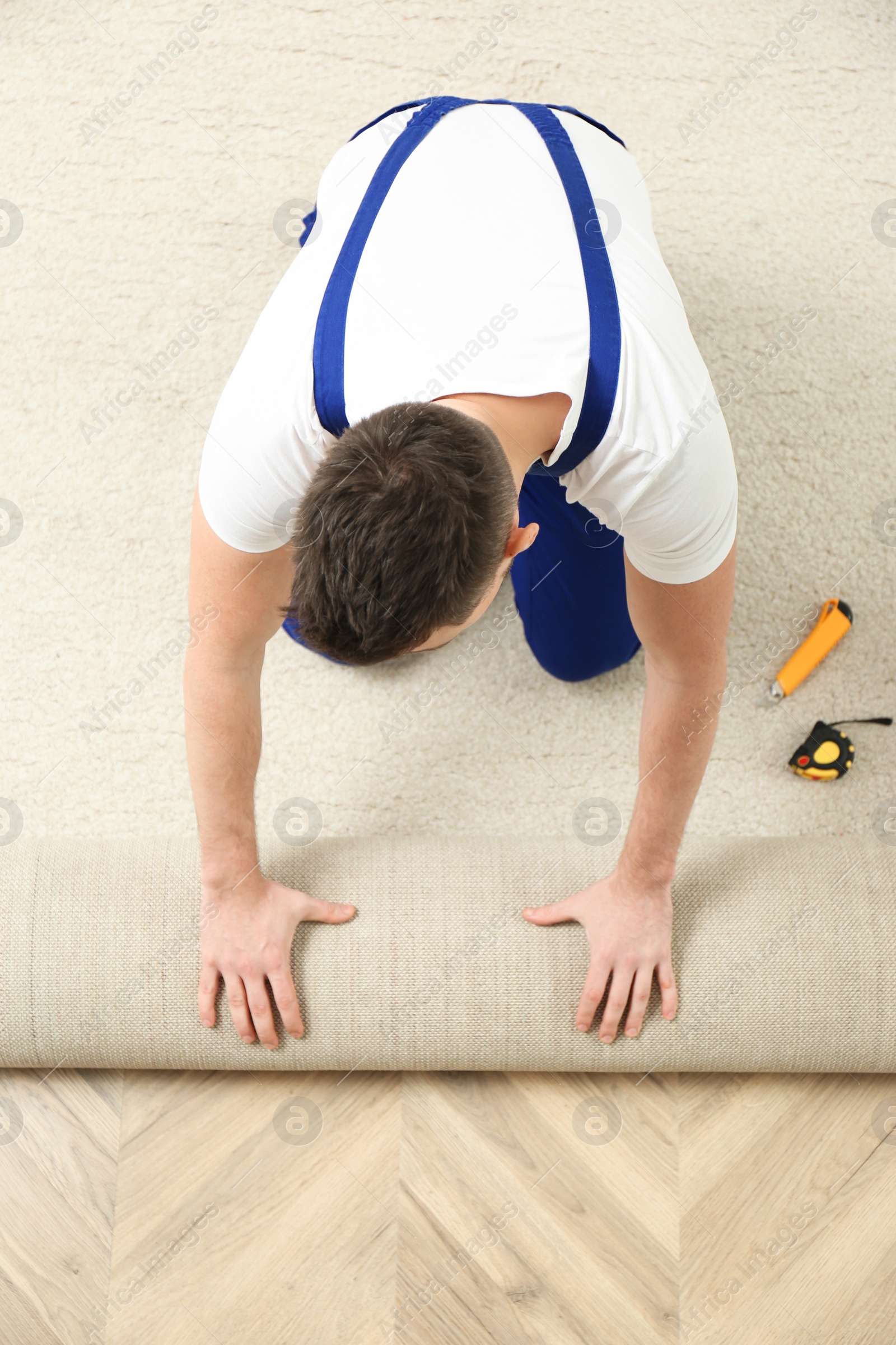 Photo of Worker rolling out new carpet flooring indoors, top view