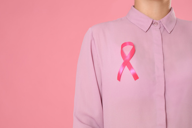 Closeup view of woman with pink ribbon on color background, space for text. Breast cancer awareness