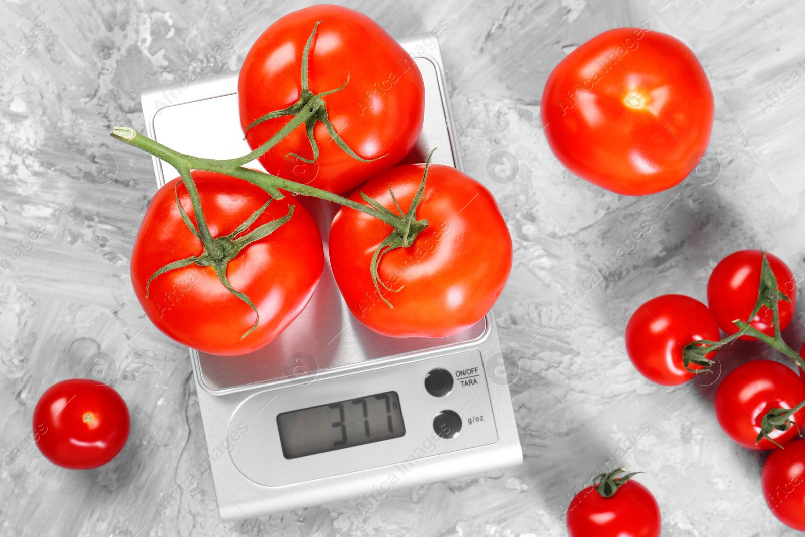 Photo of Kitchen scale with tomatoes on grey textured table, flat lay