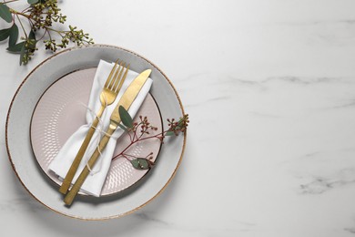 Stylish setting with cutlery and eucalyptus leaves on white marble table, flat lay. Space for text