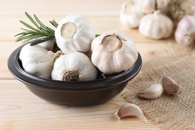 Fresh raw garlic and rosemary on wooden table, closeup