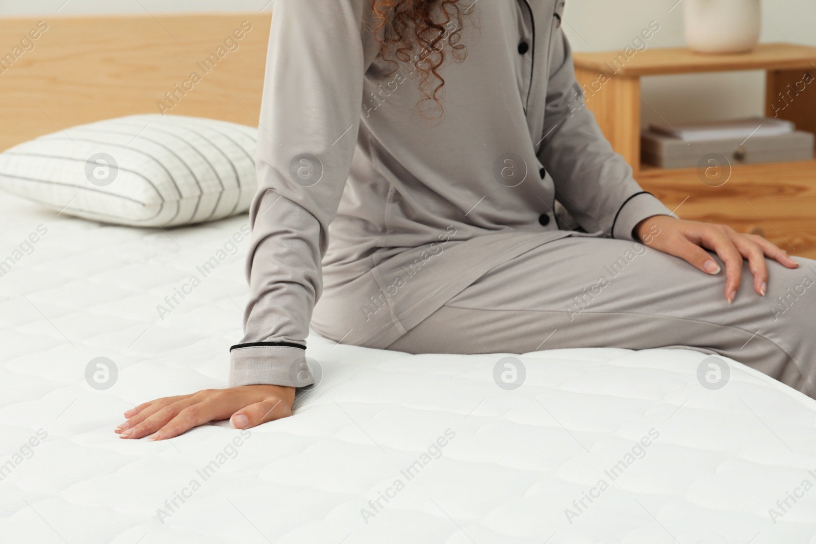 Photo of African American woman sitting on soft mattress in bedroom, closeup