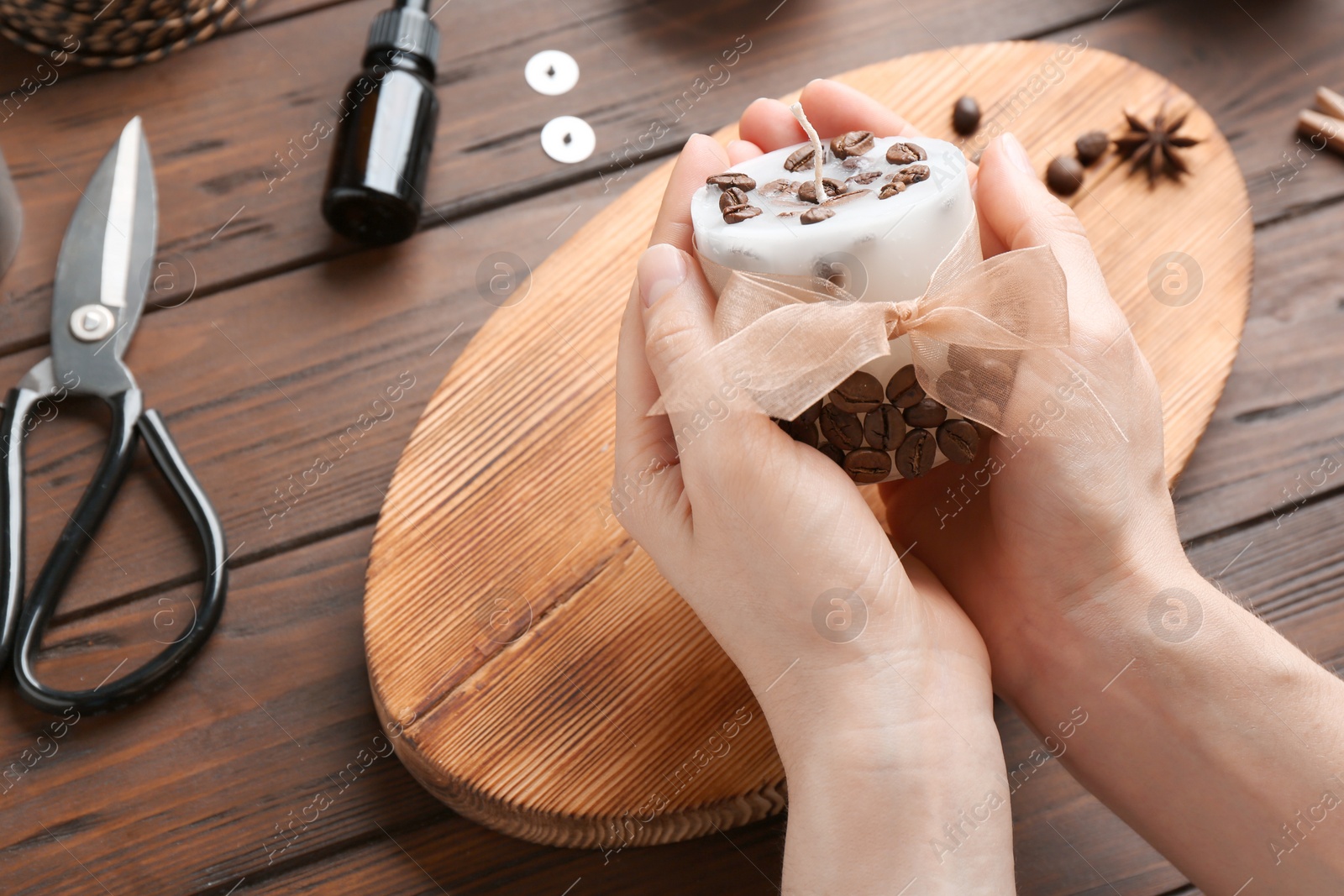 Photo of Woman holding coffee candle at wooden table, closeup