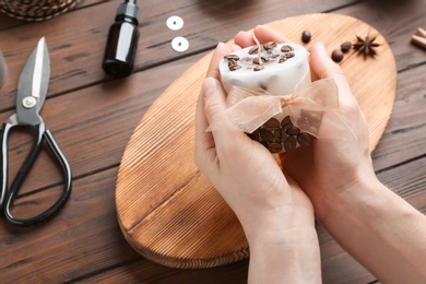 Photo of Woman holding coffee candle at wooden table, closeup