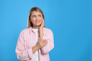Photo of Young woman suffering from ear pain on light blue background. Space for text