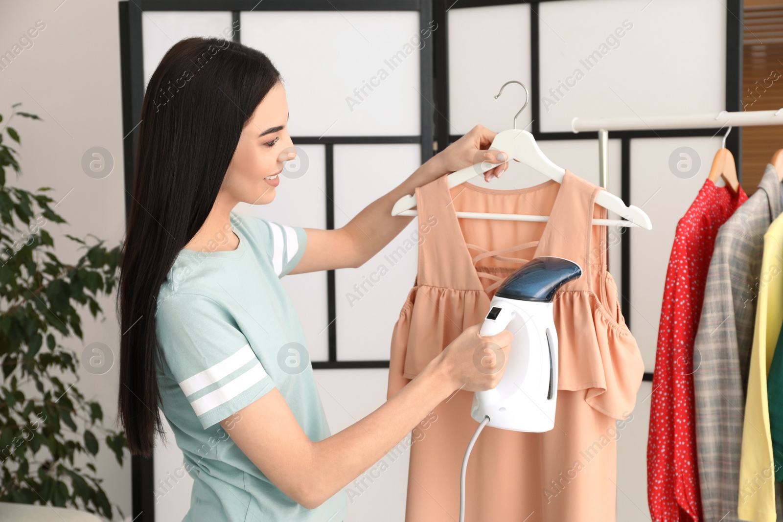 Photo of Woman steaming dress on hanger at home